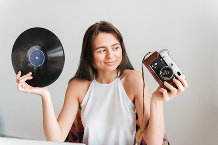 Image of cheerful happy casual woman sitting on the chair in the house while holding record and...