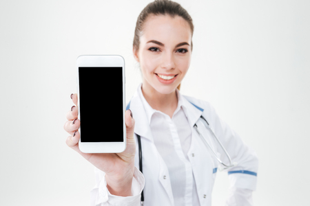 Cheerful cute young woman doctor showing blank screen mobile phone over white backgroundの写真素材