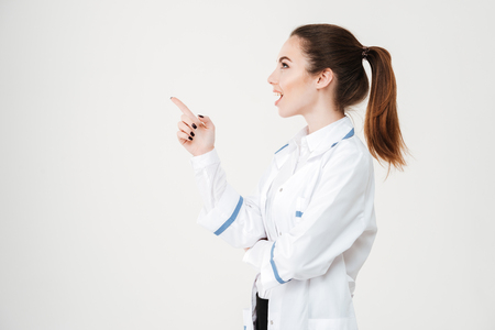Prodile of happy surprised young woman doctor looking and pointing away over white backgroundの写真素材