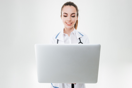 Happy charming young woman doctor using laptop computer over white backgroundの写真素材