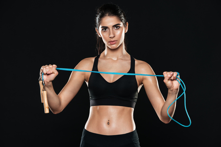 Image of fitness woman in gym standing over black background and make sport exercises holding jumping rope.の写真素材