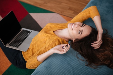 Close up portrait of a smiling attractive girl using laptop while sitting in the living roomの写真素材