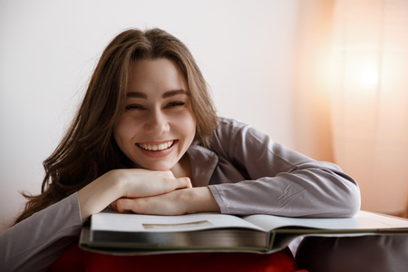Laughing woman in pajama which lying on bag chair with book while looking at cameraの写真素材