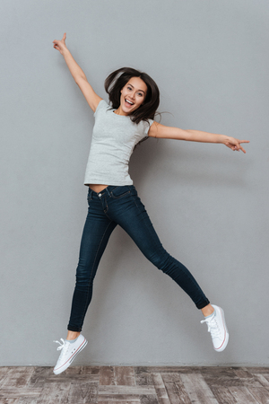 Vertical image of happy woman jumping in studio and looking at camera over gray backgroundの写真素材