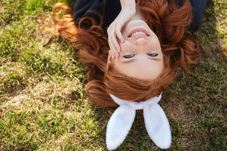 Top view close up of a smiling cheerful red head girl wearing easter bunny ears outdoorsの写真素材