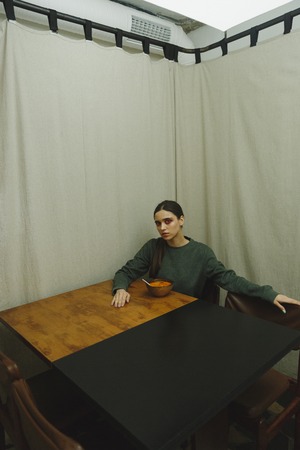 Vertical picture of a calm woman in sweater sitting by the table in eatery while looking at cameraの写真素材