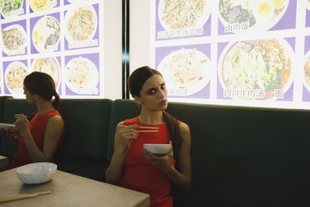 Young woman in red suit eating in eatery and looking at cameraの写真素材