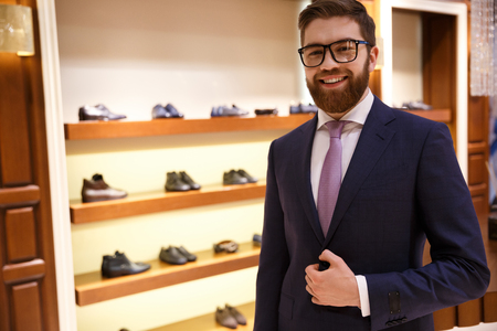 Happy businessman in suit and glasses stading near shelf with shoesの写真素材