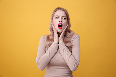 Image of shocked young blonde lady with bright makeup lips posing over yellow background. Looking aside.の写真素材