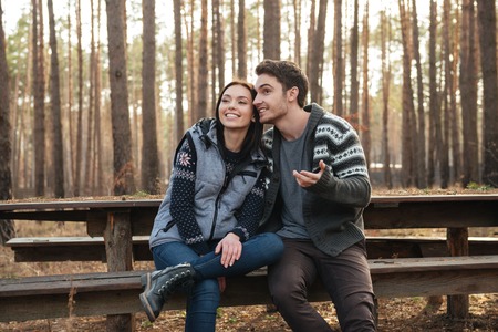 Young pretty man and woman sitting on bench and talking in forestの写真素材