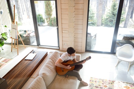 topview of young brunette man playing guitar on couchの写真素材
