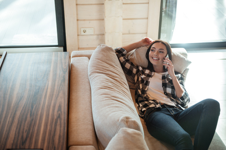 Pretty woman lying on soft couch and talking on phoneの写真素材