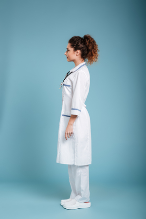Full lenght side view photo of a concentrated young nurse with stethoscope looking aside isolated over blue background.の写真素材