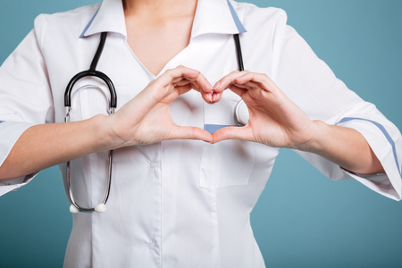 Close up portrait of a nurse with stethoscope showing heart gesture with hands isolated on blueの写真素材