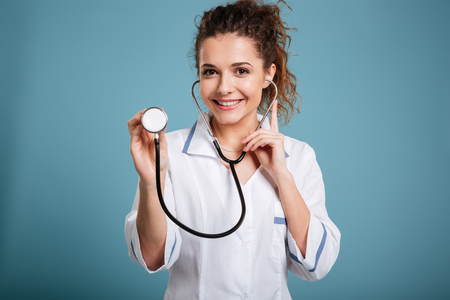 Portrait of a young smiling nurse holding stethoscope isolated on blue backgroundの写真素材