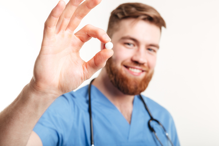 Portrait of a smiling young male medical doctor offering a pill on white backgroundの写真素材