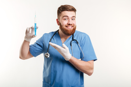 Portrait of a happy attractive medical doctor or nurse pointing han at syringe and looking at camera isolated on white backgroundの写真素材
