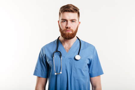 Portrait of a serious confident male doctor standing over white backgroundの写真素材