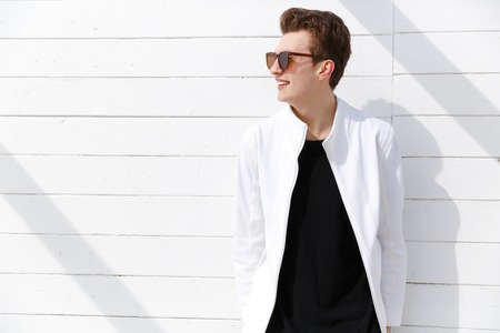 Portrait of smiling young man in sunglasses over white wall backgroundの写真素材