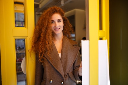 Trendy young smiling woman walking out of a coffee shopの写真素材
