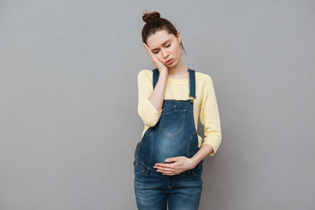 Image of tired pregnant woman posing isolated over grey wall. Eyes closed.の写真素材