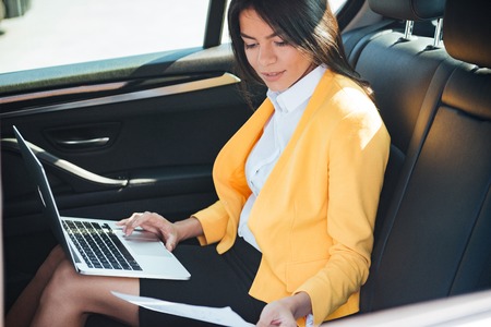 Portrait of a young businesswoman working with laptop on back seat in carの写真素材