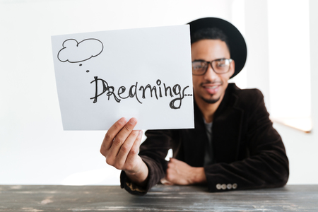 Young African man showing sheet of paper with word at camera. Focus on paperの写真素材