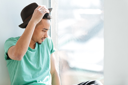 African man in green t-shirt and hat sitting near the windowの写真素材