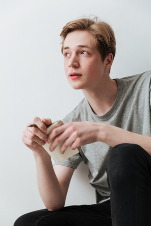 Vertical image of a pensive man sitting in studio and holding notebook in hands over gray backgroundの写真素材