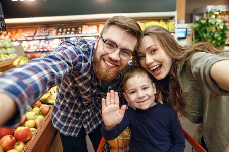 Happy young family posing in supermarket and looking at the cameraの写真素材