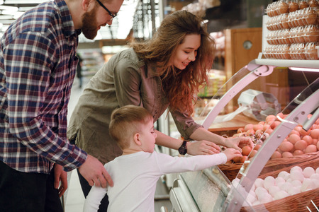 Side view of a happy family choosing eggs in supermarketの写真素材
