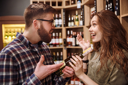 Side view of a Surprised happy couple choosing bottle of wine in supermarketの写真素材