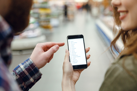 Cropped image of a couple looking at smartphone while being in supermarket. View from backの写真素材