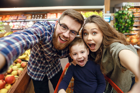 Happy young family making photo in supermarket and looking at the cameraの写真素材
