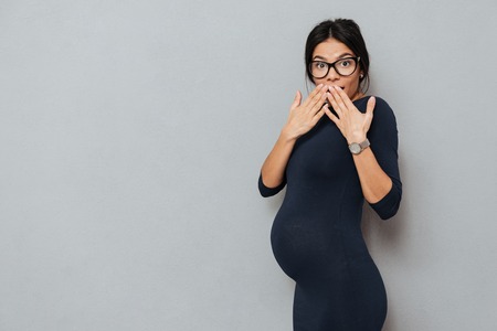 Photo of surprised emotional pregnant business lady standing over grey background. Looking at camera.の写真素材