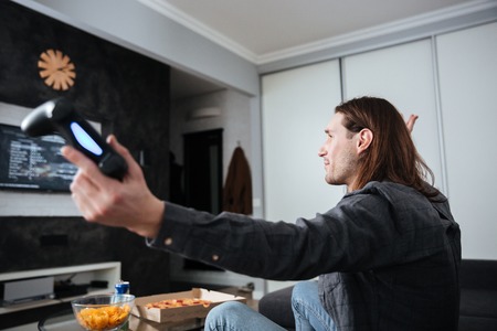 Side view image of young sad man gamer sitting at home indoors and play games with joystick.の写真素材