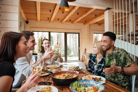 Group of cheerful young friends having dinner and laughing at the table at home