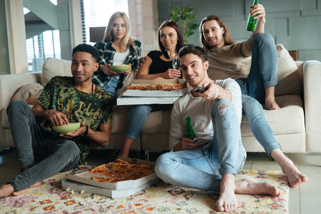 Image of a five friends with pizza and beer sitting in house and watching TVの写真素材