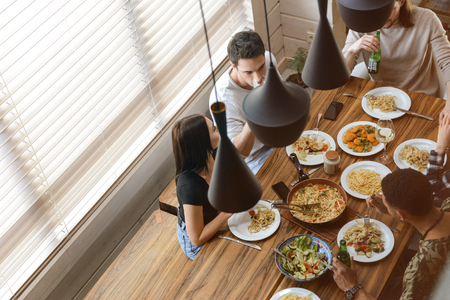 Top view of group of happy young friends sitting at the table and having dinner on the kitchenの写真素材