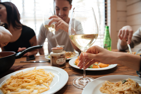 Closeup of group of people drinking wine and eating pasta at the table at homeの写真素材
