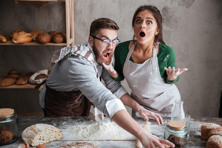 Shocked man and suprised woman trying to catch something on table with productsの写真素材