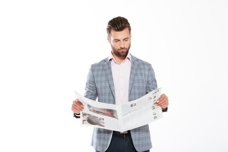 Picture of concentrated young man standing isolated over white background and reading gazette. Looking aside.の写真素材