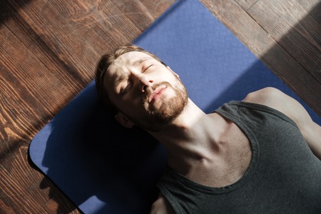 Image of concentrated young strong sportsman in gym lies on floor with eyes closed.の写真素材