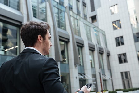Back view of busy businessman with smartphone in large modern building