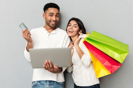 Happy woman with packasges and african man with credit card and laptop looking cameraの写真素材