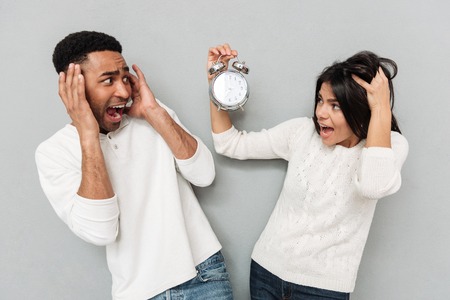 Picture of young screaming confused loving couple standing over grey wall and showing alarm. Looking...