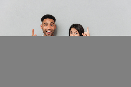 Picture of young cheerful loving couple standing over grey wall and using laptop computer. Looking at camera have an idea.の写真素材