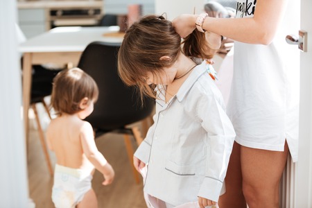 Closeup of mother standing and doing hair to her little daughter at homeの写真素材