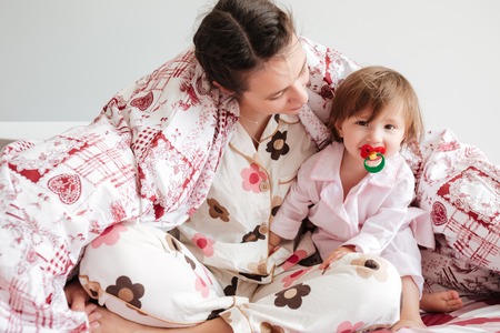Young womam mother sitting in bed in blanket with her cute daughterの写真素材