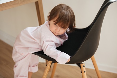 Cute little girl in pajamas climbing on chair at homeの写真素材